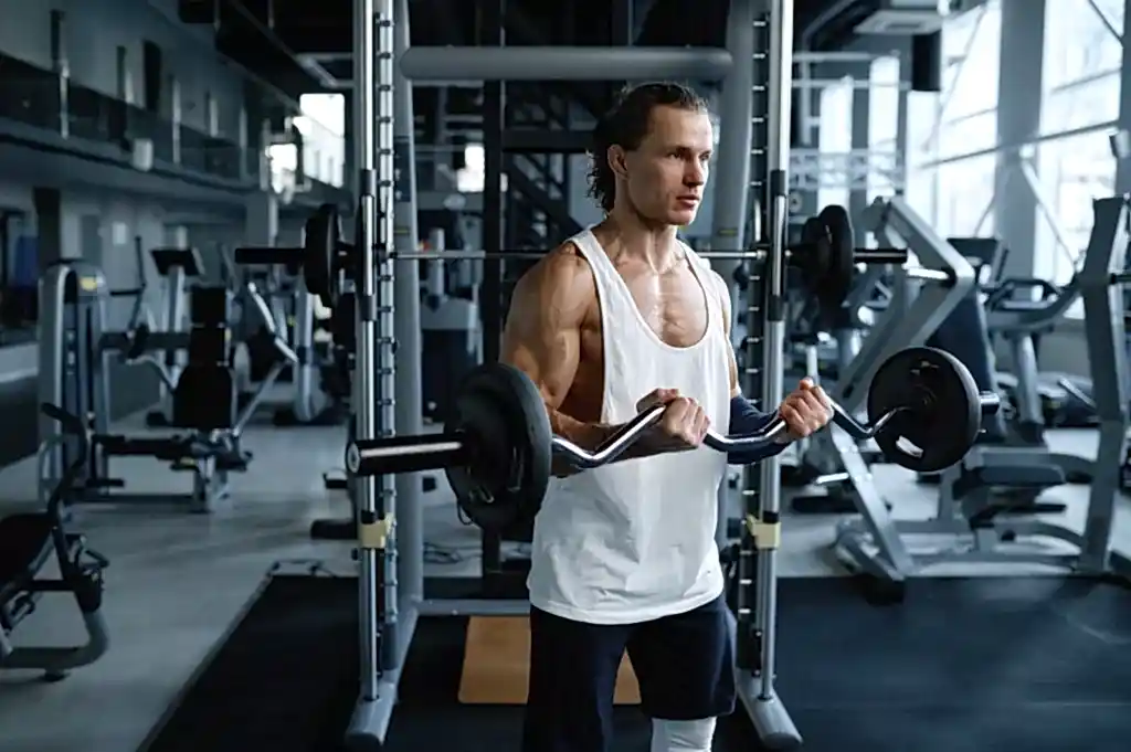 Man athlete training muscles with barbell during physical workout in sport gym