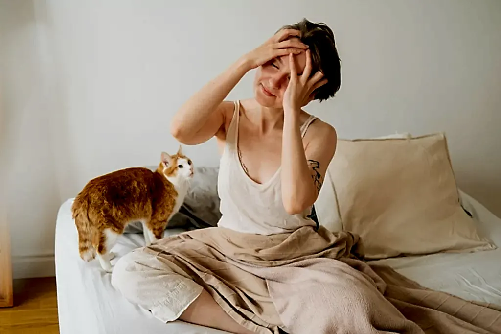 Young woman holds her head while sitting on the bed. Morning migraine concept.